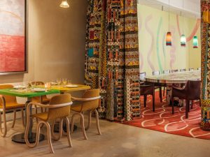 Table set for four next to a colorful curtain that opens up into a pirvate dining area with a long communal table.