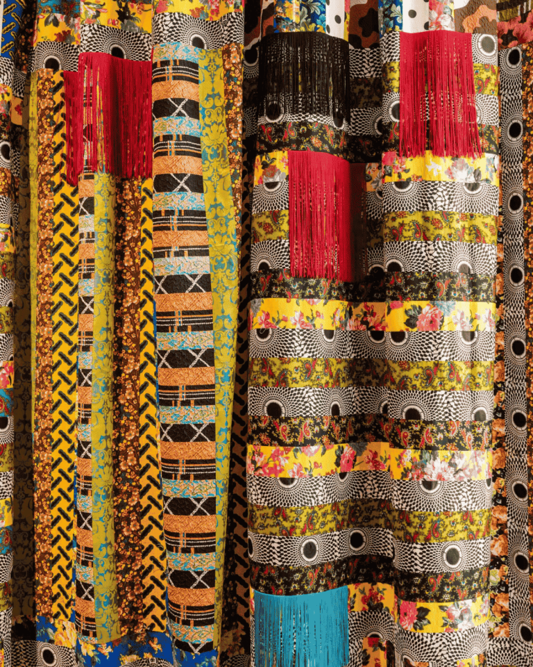 A curtain of multiple fabrics sewn together with contracting patterns and colors. The curtain was created by Duro Olowu.