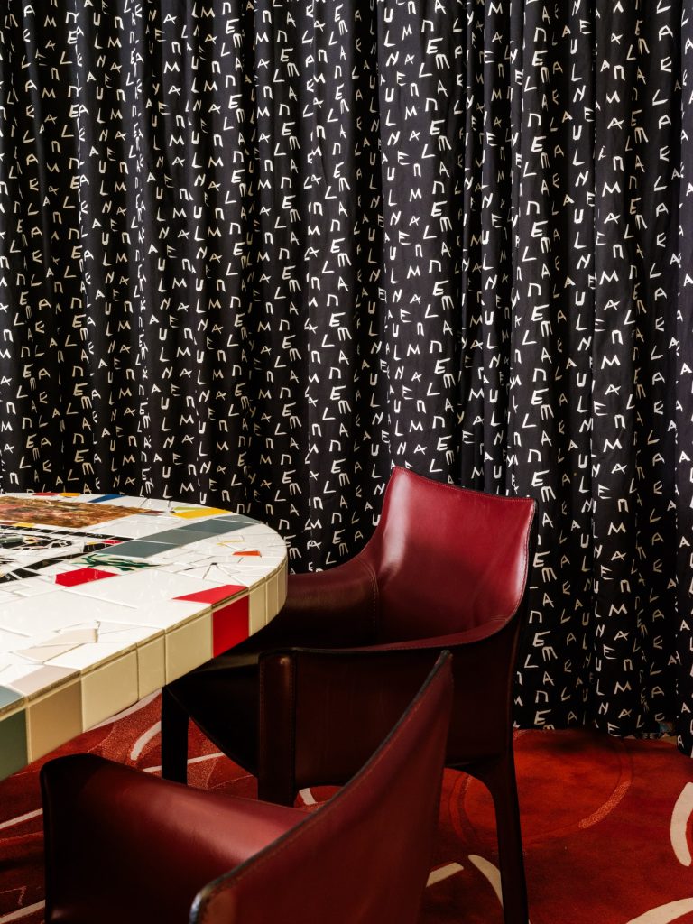 Interior image of the private dining room with black curtain. There is a corner of a table top with a mosaic and oxblood chairs.