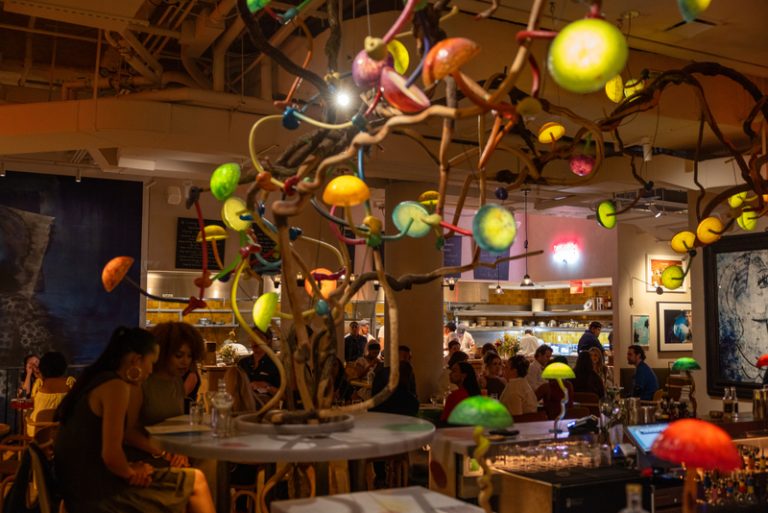 Life at Manuela Lively restaurant interior with people enjoying dinner. A chandelier with multicolored mushroom lights hangs from the ceiling.