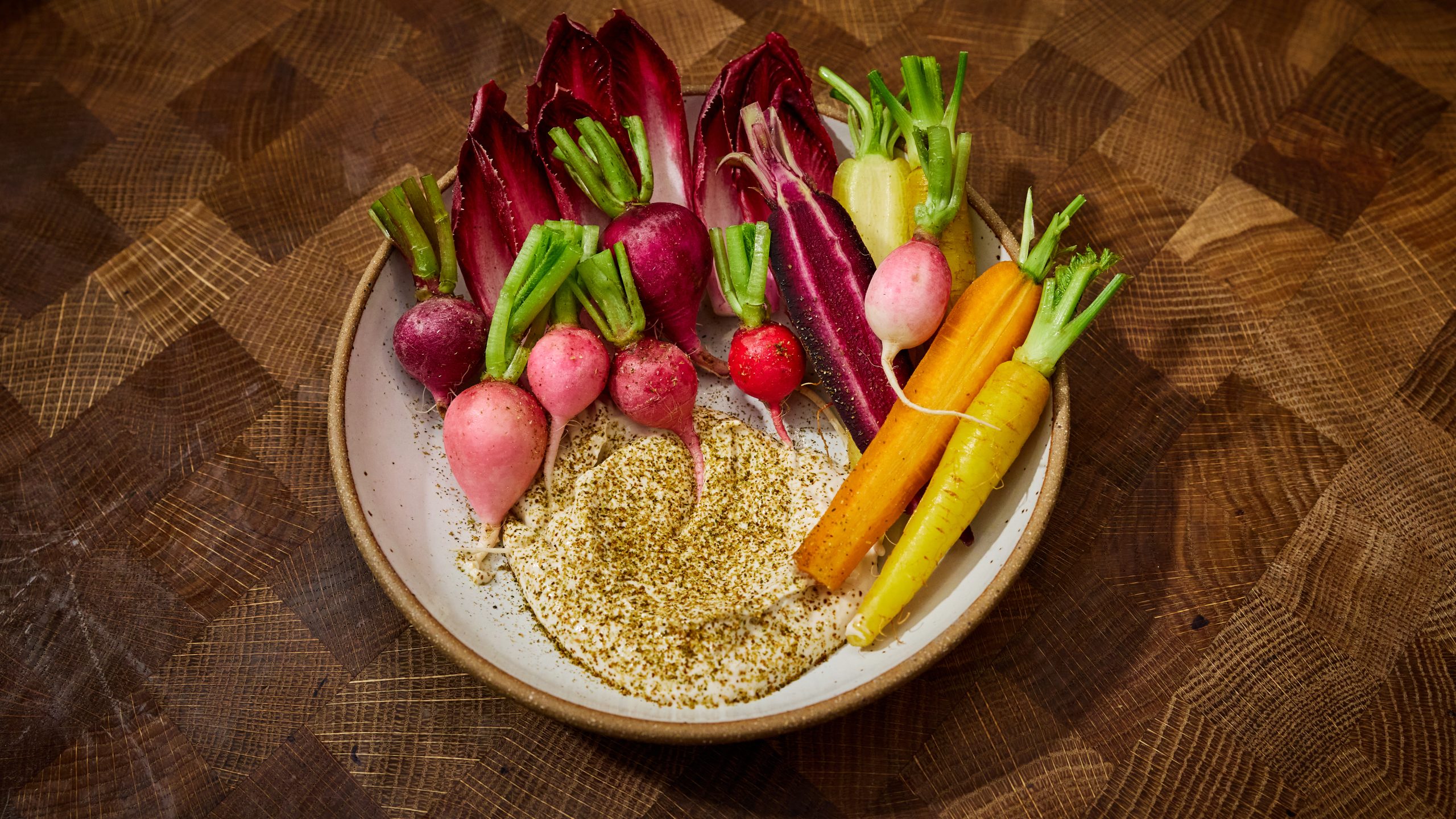 A bowl of fresh carrots and radishes next to a beige dip.