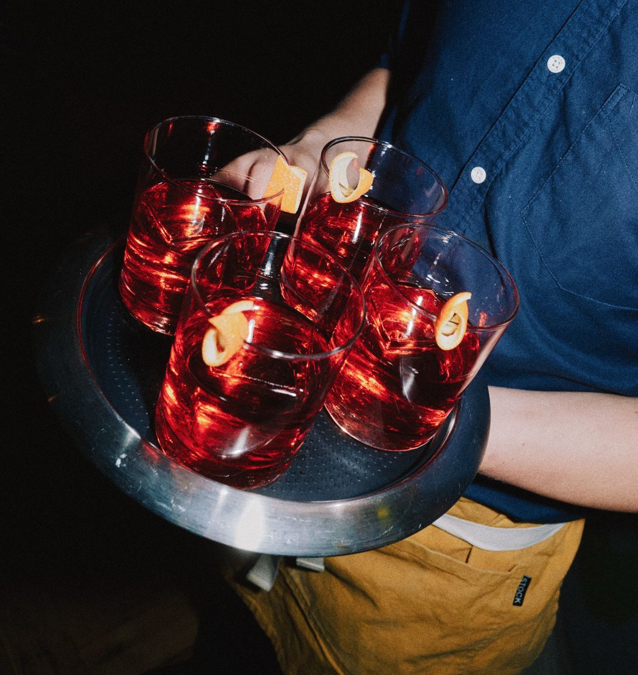server in blue shirt carrying a tray of red Negroni cocktails