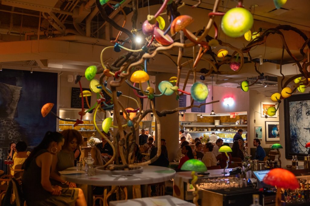 Restaurant interior with an assortment of colorful mushroom shaped lights hanging from the ceiling while people are eating dinner.