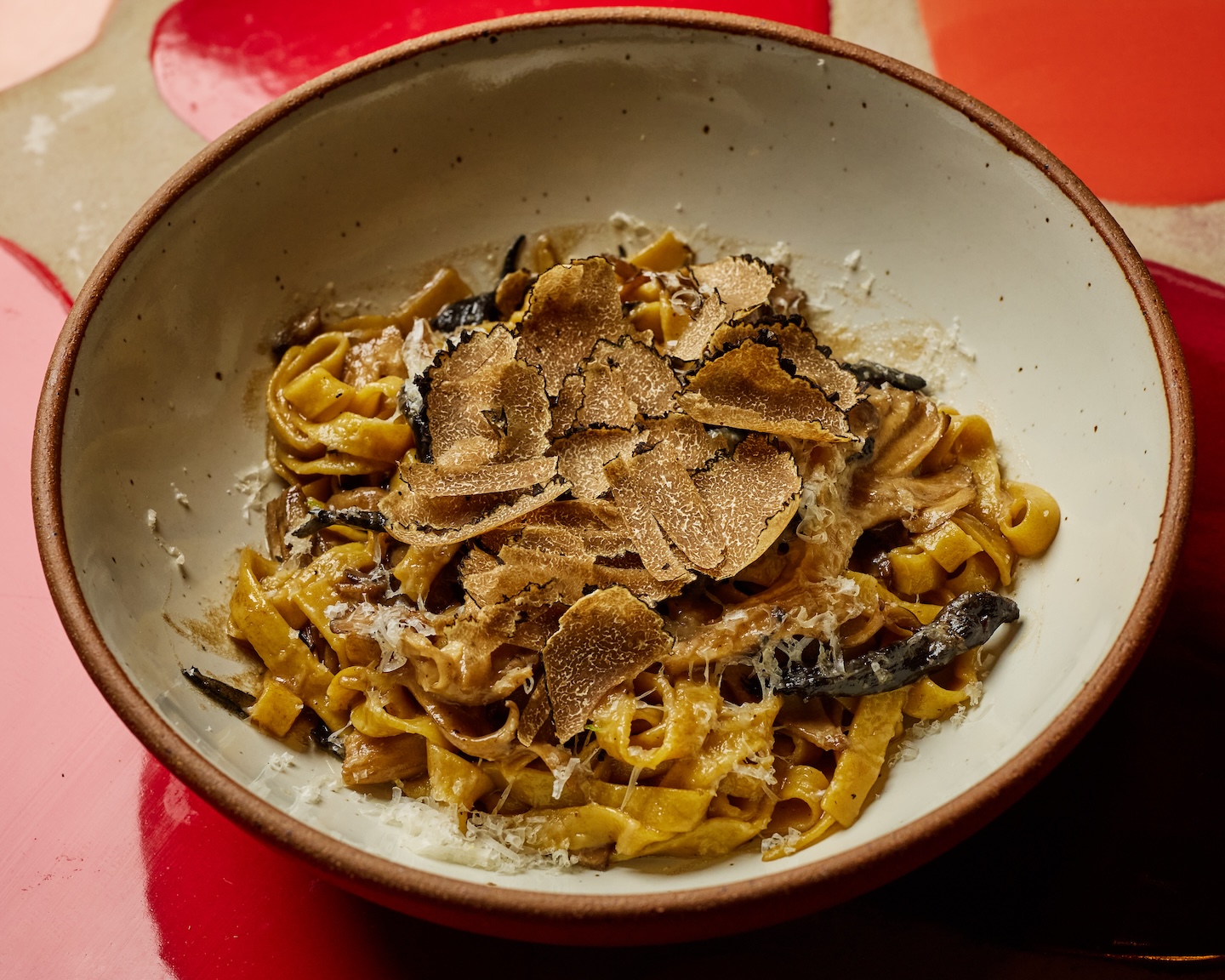 Beige bowl fill of flat, long pasta topped with truffle slices.