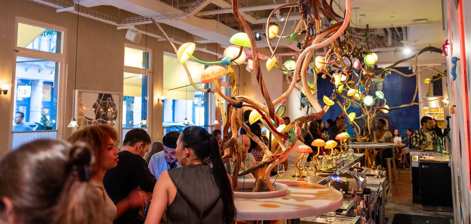 An interior of a restaurant with people sitting and enjoying a meal. Abstract chandeliers hang from the ceiling.