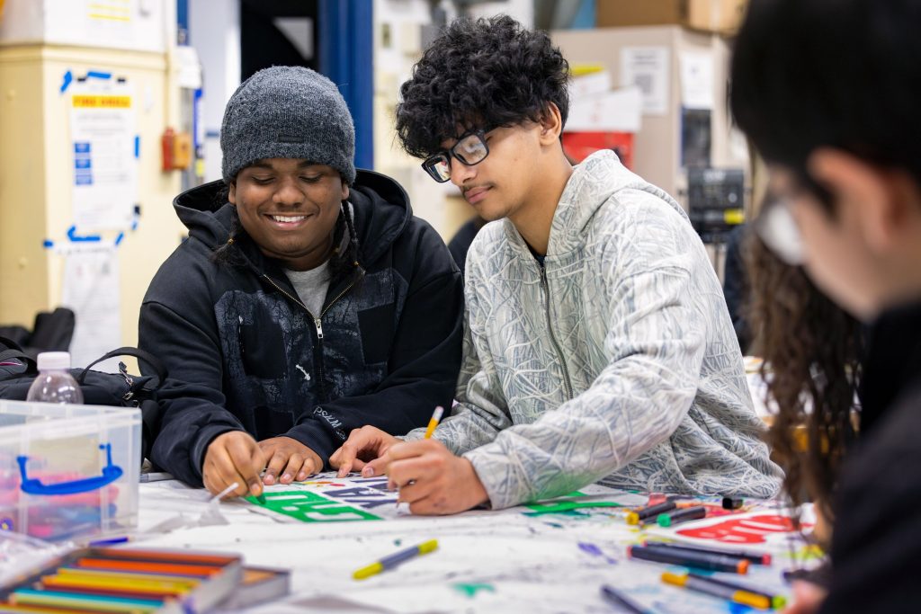 Allison Katz Poster Project – a colourful poster being illustrated by two male students