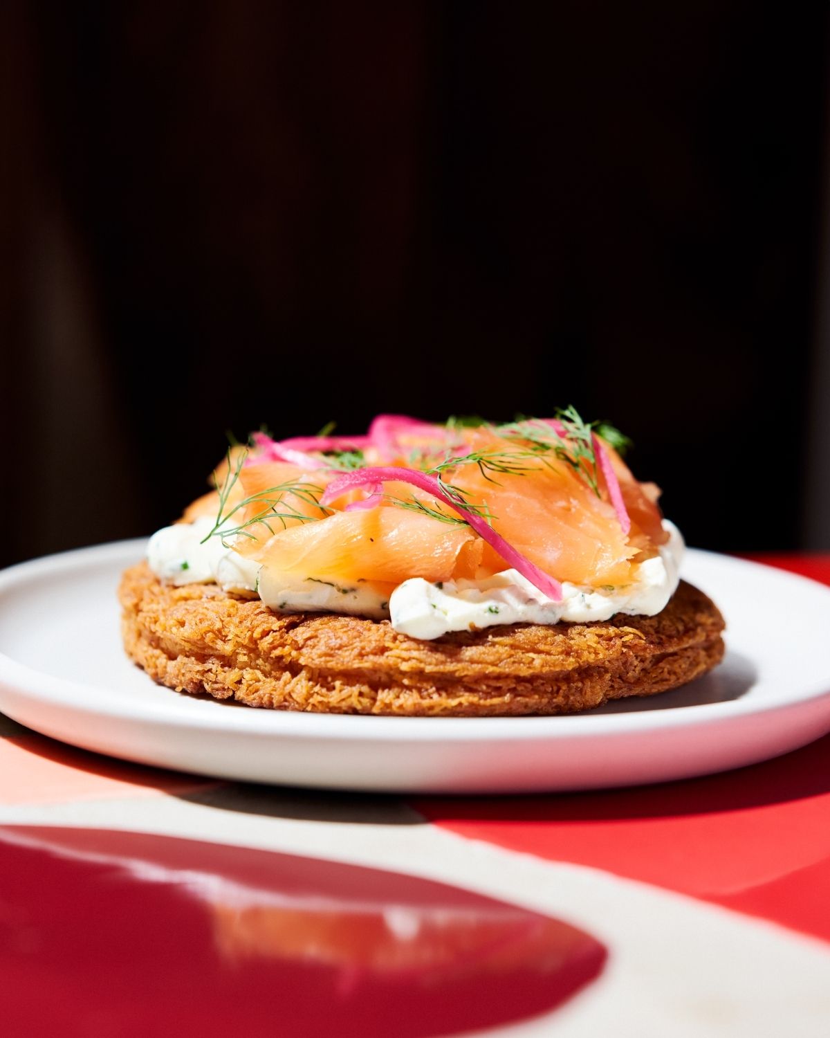Crispy savoury tart topped with smoked fish, cream and pickled vegetables on a white plate